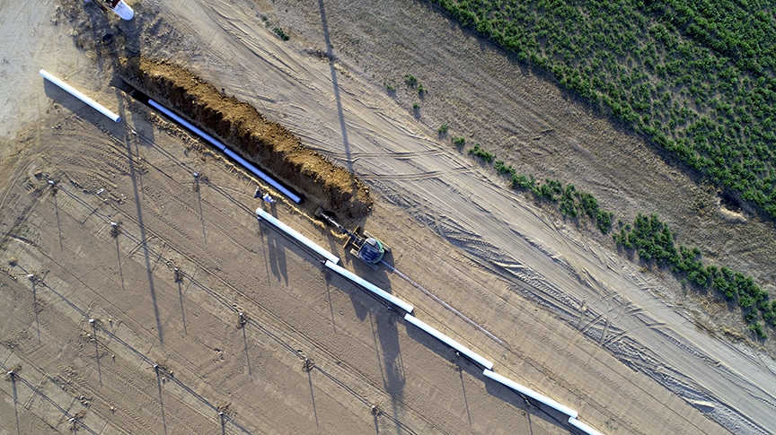 Placing Piping in the Ground With Dusty Road on Either Side of Pipes